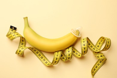 Photo of Sex education. Banana with measuring tape and condom on beige background, flat lay