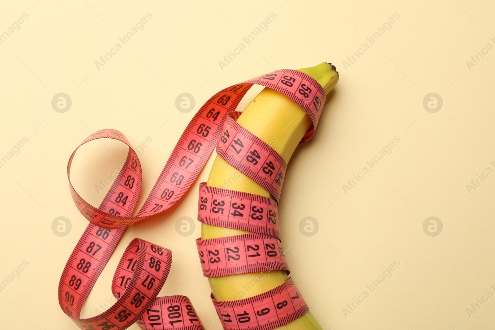 Sex education. Banana with measuring tape on beige background, top view Photo of Sex education. Banana with measuring tape on beige background, top view