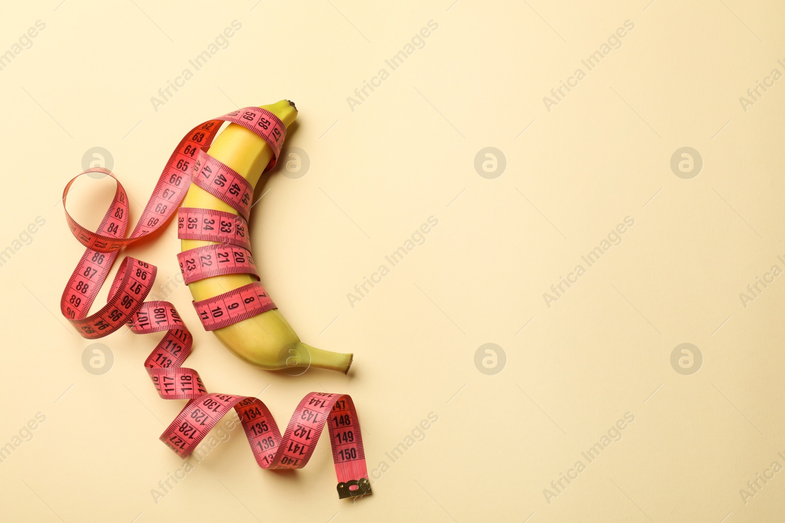 Sex education. Banana with measuring tape on beige background, top view. Space for text Photo of Sex education. Banana with measuring tape on beige background, top view. Space for text