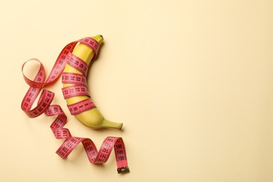 Photo of Sex education. Banana with measuring tape on beige background, top view. Space for text