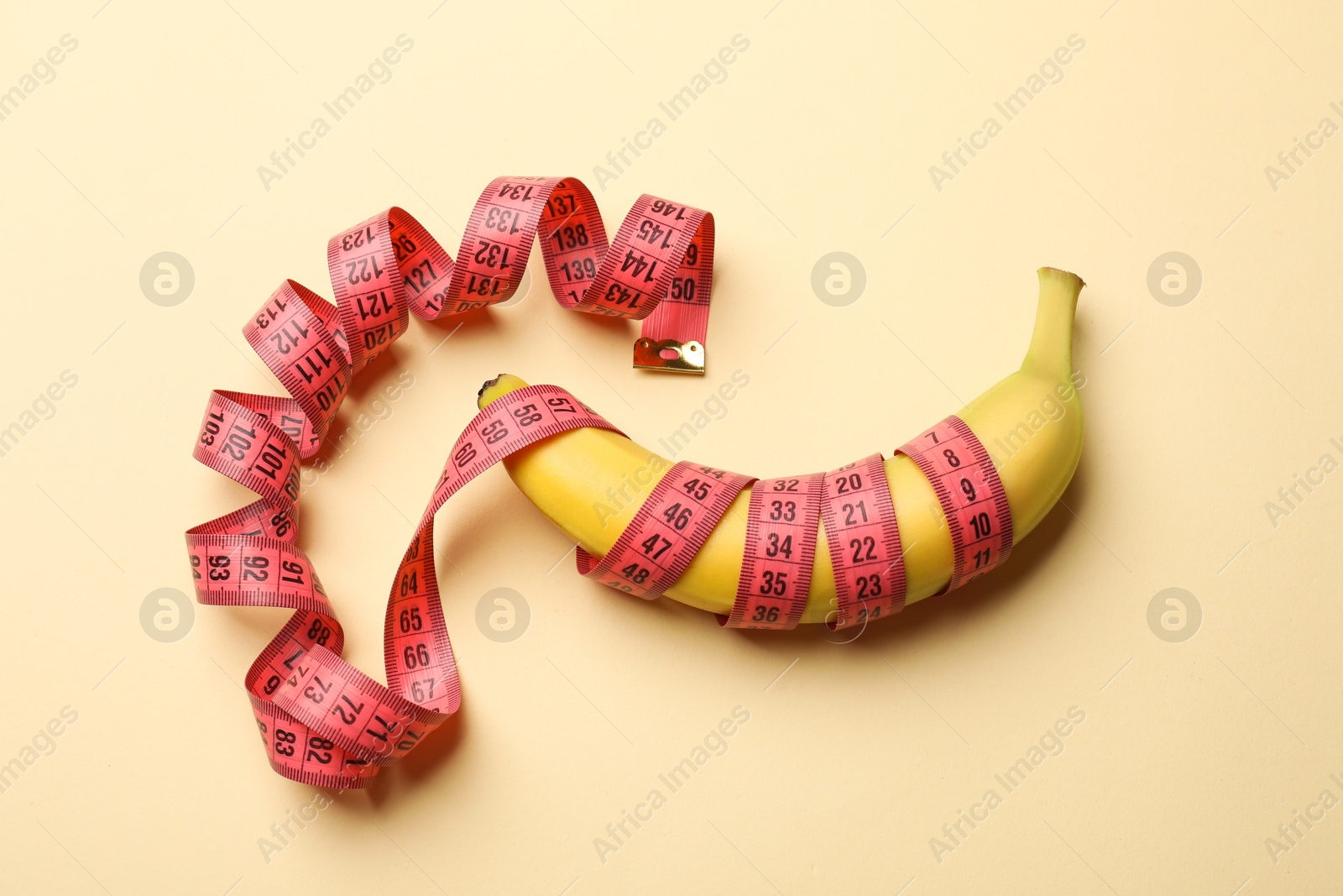 Sex education. Banana with measuring tape on beige background, top view Photo of Sex education. Banana with measuring tape on beige background, top view