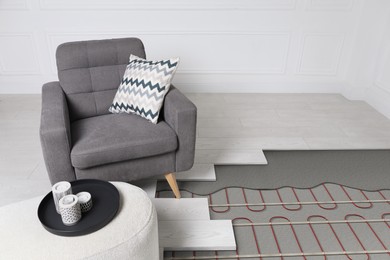 Image of Underfloor heating system installed in room with armchair and pouf. Pipes seen under laminate