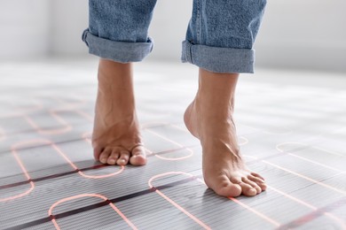 Image of Woman walking barefoot on warm floor at home, closeup. Underfloor heating system seen through laminate