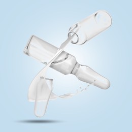 Image of Ampoules and splash of medical or cosmetic liquid in air against light blue background