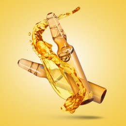 Image of Ampoules and splash of medical or cosmetic liquid in air against golden background