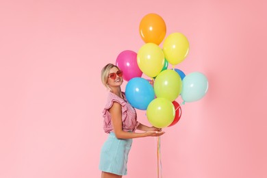 Photo of Smiling woman in sunglasses with bunch of colorful balloons on pink background