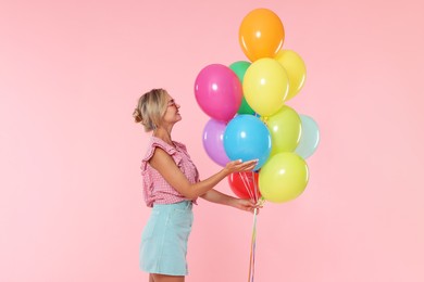 Photo of Smiling woman in sunglasses with bunch of colorful balloons on pink background