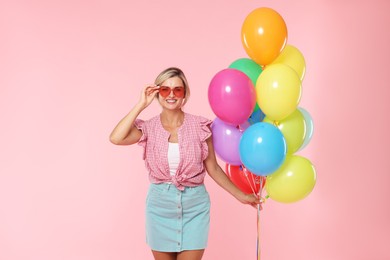 Photo of Smiling woman in sunglasses with bunch of colorful balloons on pink background