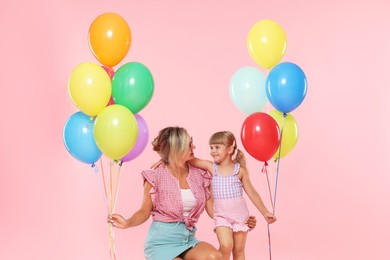 Photo of Happy mother in sunglasses and her little daughter with bunches of colorful balloons on pink background