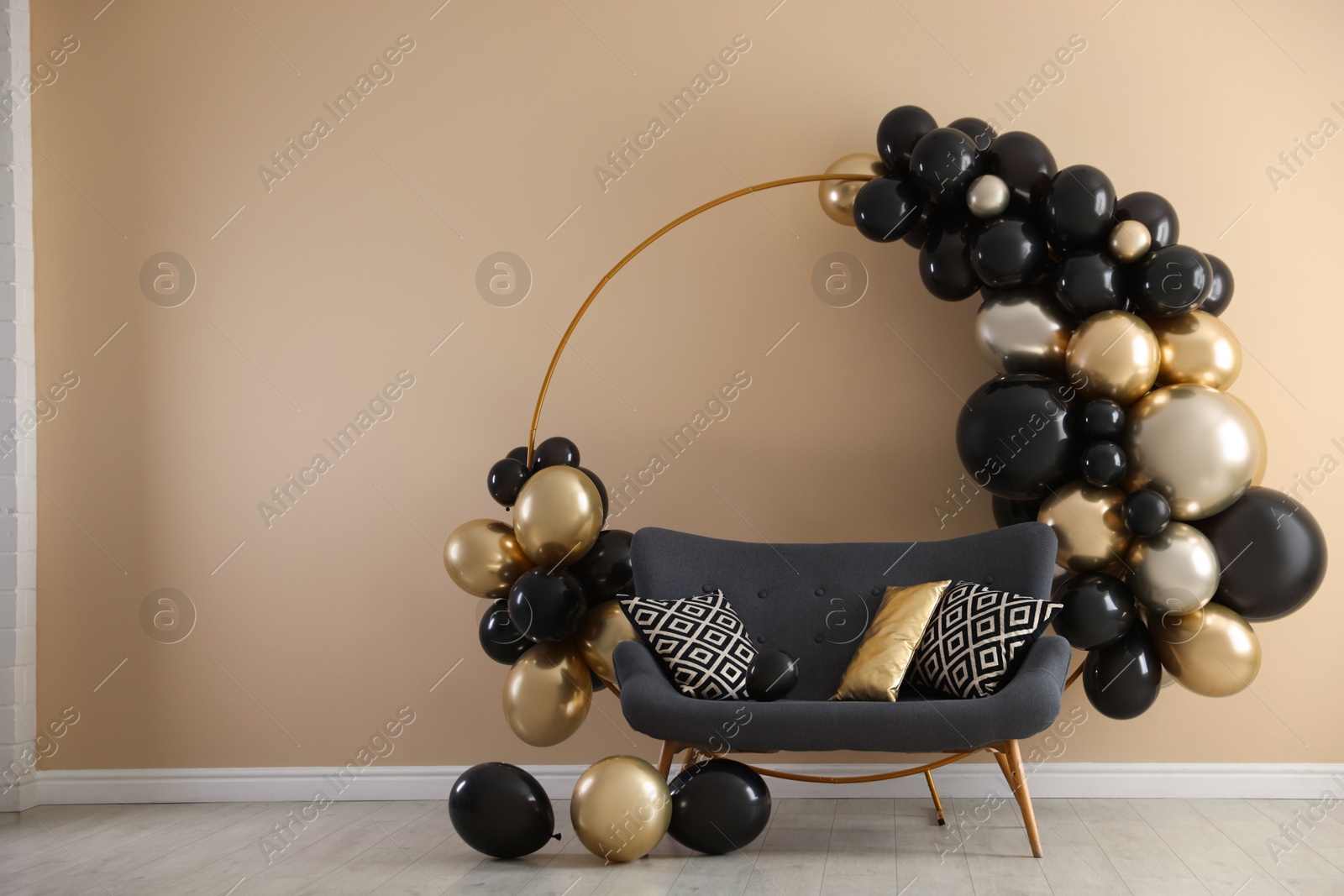 Photo of Stylish photo zone with balloons and sofa near beige wall. Space for text