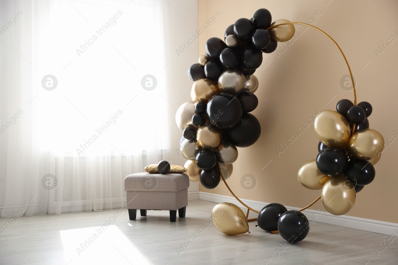 Stylish photo zone with balloons and pouf near beige wall Photo of Stylish photo zone with balloons and pouf near beige wall