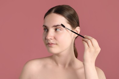 Photo of Young woman brushing her eyebrow with spoolie on pink background