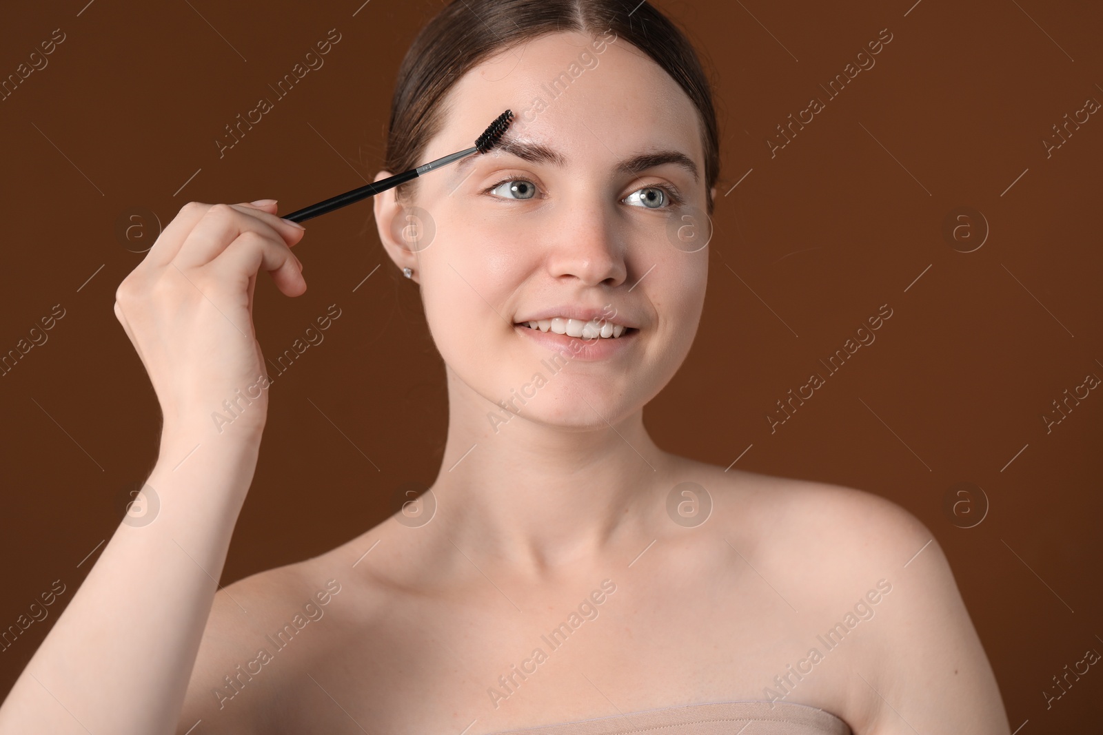 Photo of Young woman brushing her eyebrow with spoolie on brown background