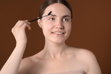 Photo of Young woman brushing her eyebrow with spoolie on brown background