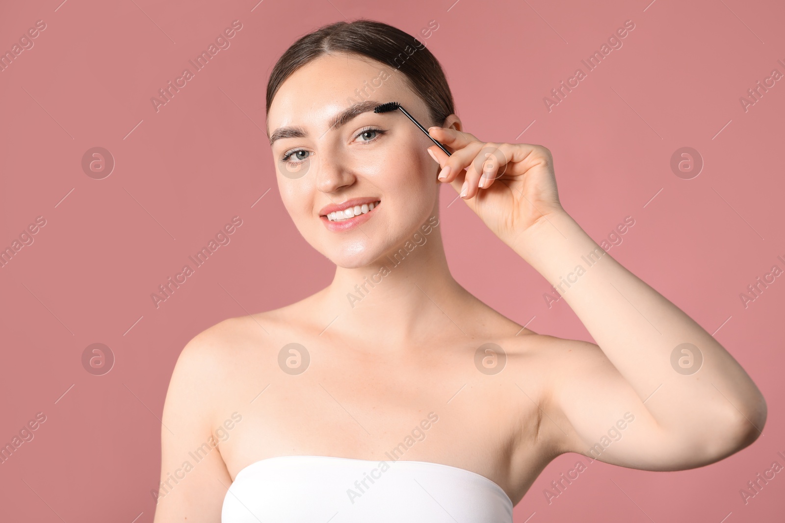 Photo of Young woman brushing her eyebrow with spoolie on pink background