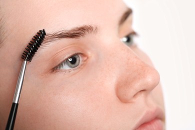 Photo of Young woman brushing her eyebrow with spoolie on white background, closeup