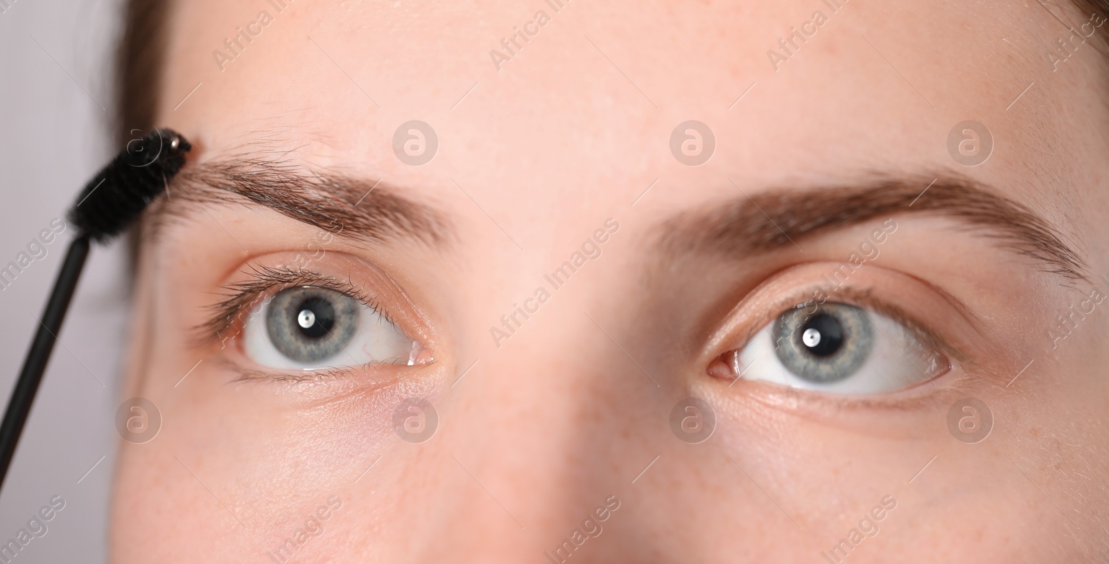 Photo of Young woman brushing her eyebrow with spoolie on light grey background, closeup
