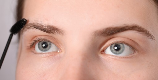 Photo of Young woman brushing her eyebrow with spoolie on light grey background, closeup