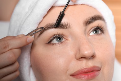 Photo of Cosmetologist plucking and brushing young woman's eyebrow, closeup