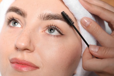 Photo of Cosmetologist brushing young woman's eyebrow with spoolie, closeup