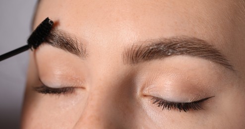 Photo of Young woman brushing her eyebrow with spoolie on light grey background, closeup