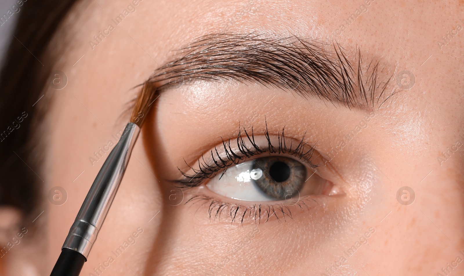 Photo of Young woman applying cosmetic product onto her eyebrow with brush, closeup