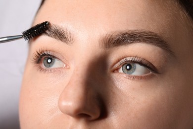 Photo of Young woman brushing her eyebrow with spoolie on light grey background, closeup