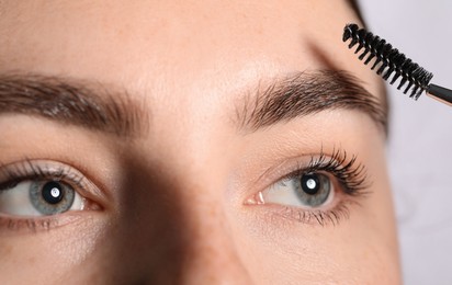 Photo of Young woman brushing her eyebrow with spoolie on light grey background, closeup