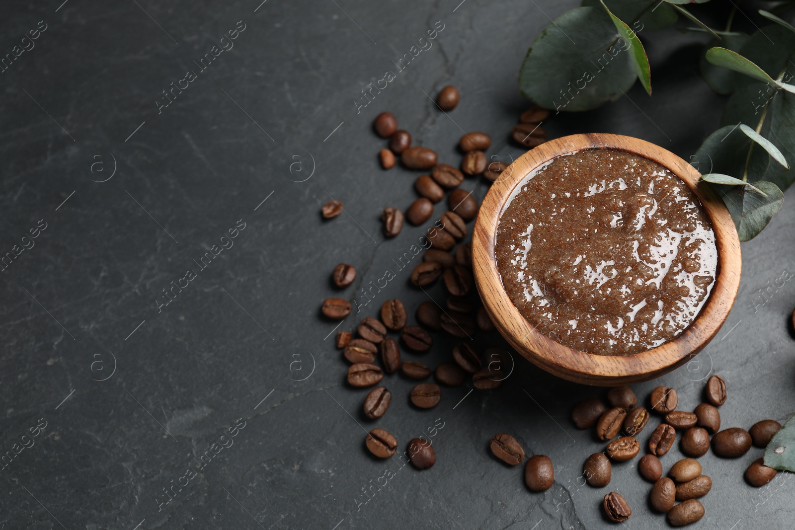 Photo of Natural body scrub, coffee beans and eucalyptus leaves on black table, flat lay. Space for text