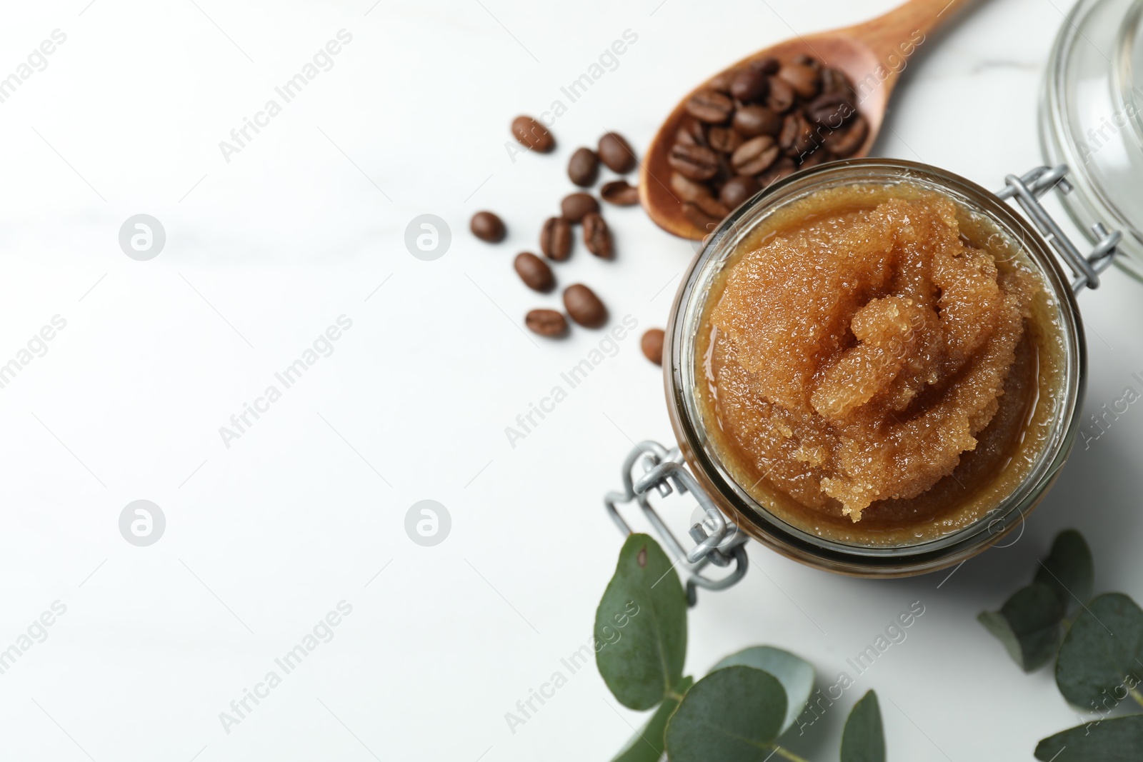 Natural body scrub, coffee beans and eucalyptus leaves on white table, flat lay. Space for text Photo of Natural body scrub, coffee beans and eucalyptus leaves on white table, flat lay. Space for text