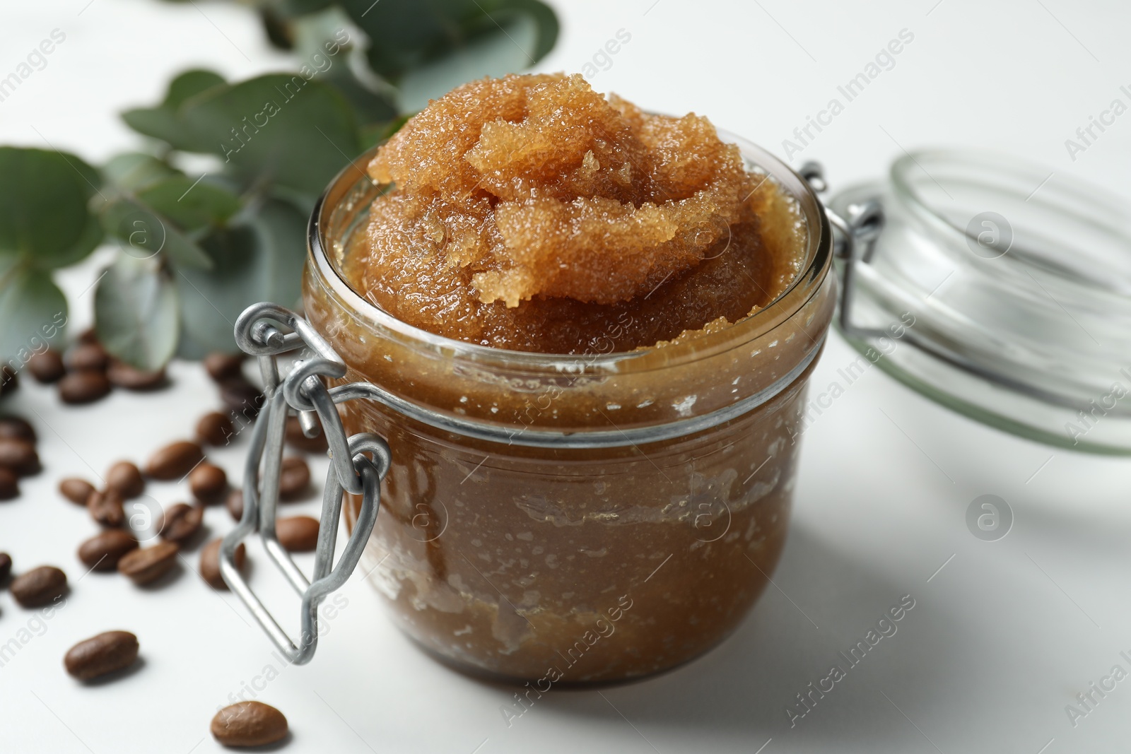 Natural body scrub, coffee beans and eucalyptus leaves on white table, closeup Photo of Natural body scrub, coffee beans and eucalyptus leaves on white table, closeup