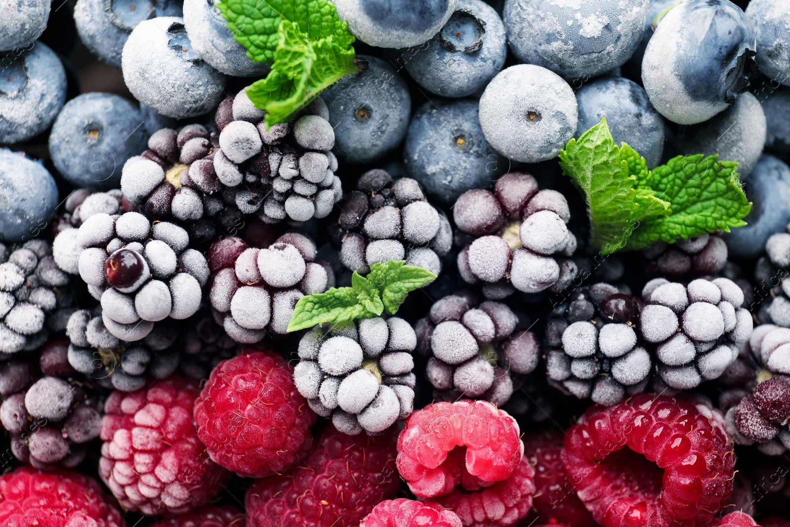 Photo of Many different frozen berries and mint as background, top view
