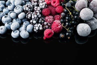 Photo of Many different frozen berries on black table, closeup. Space for text