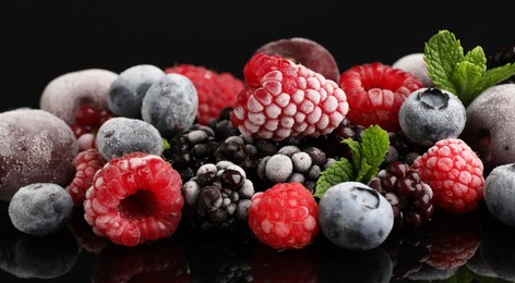 Photo of Many different frozen berries and mint on black table, closeup