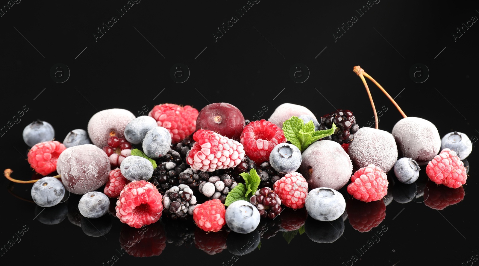 Photo of Many different frozen berries and mint on black table
