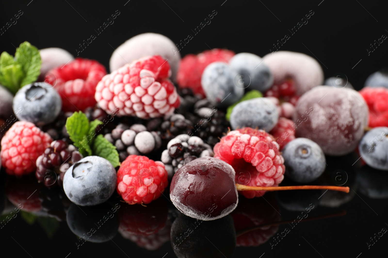 Photo of Many different frozen berries and mint on black table, closeup