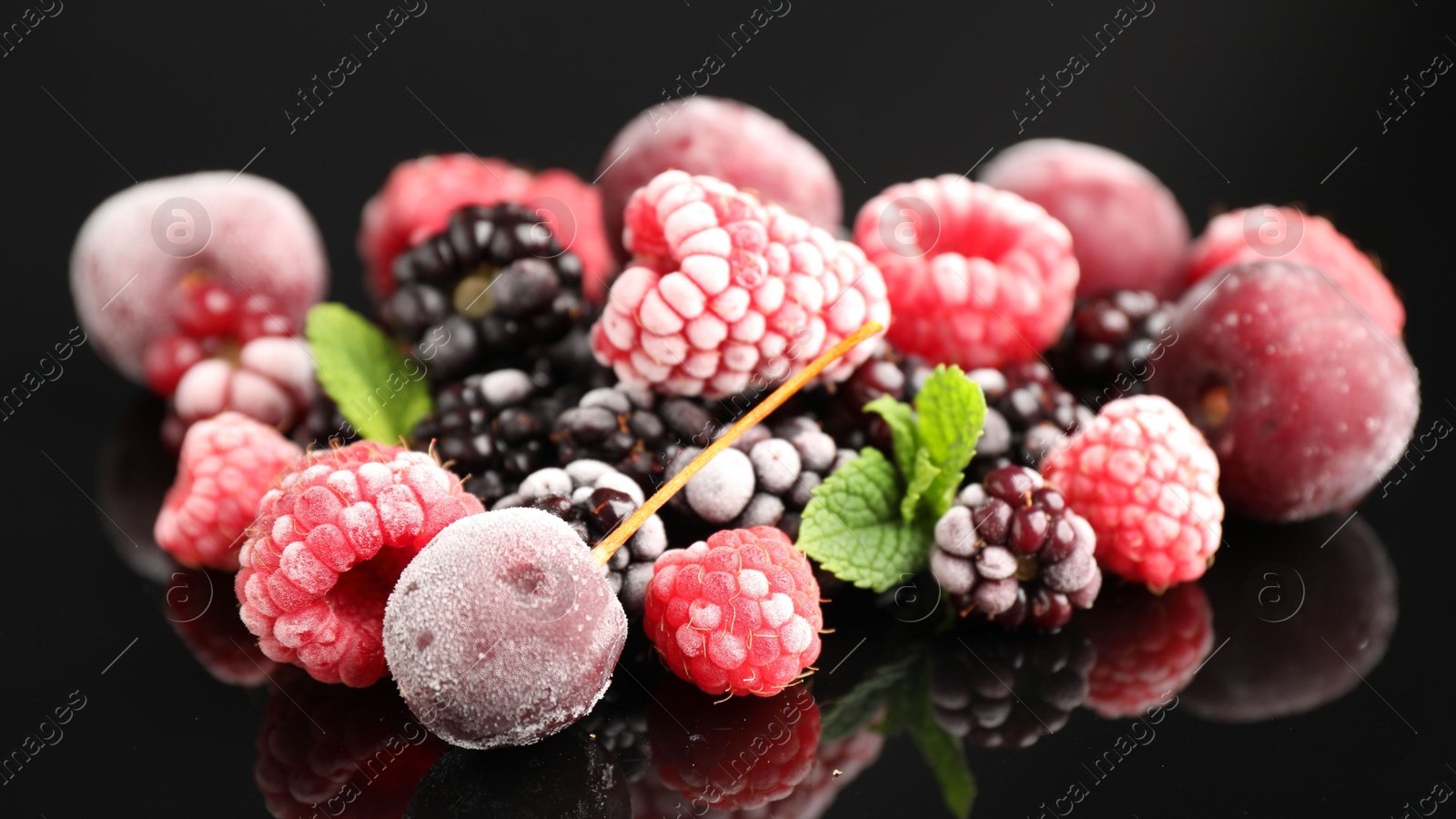 Photo of Many different frozen berries and mint on black table, closeup