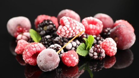 Photo of Many different frozen berries and mint on black table, closeup