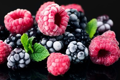 Photo of Many different frozen berries and mint on black table, closeup