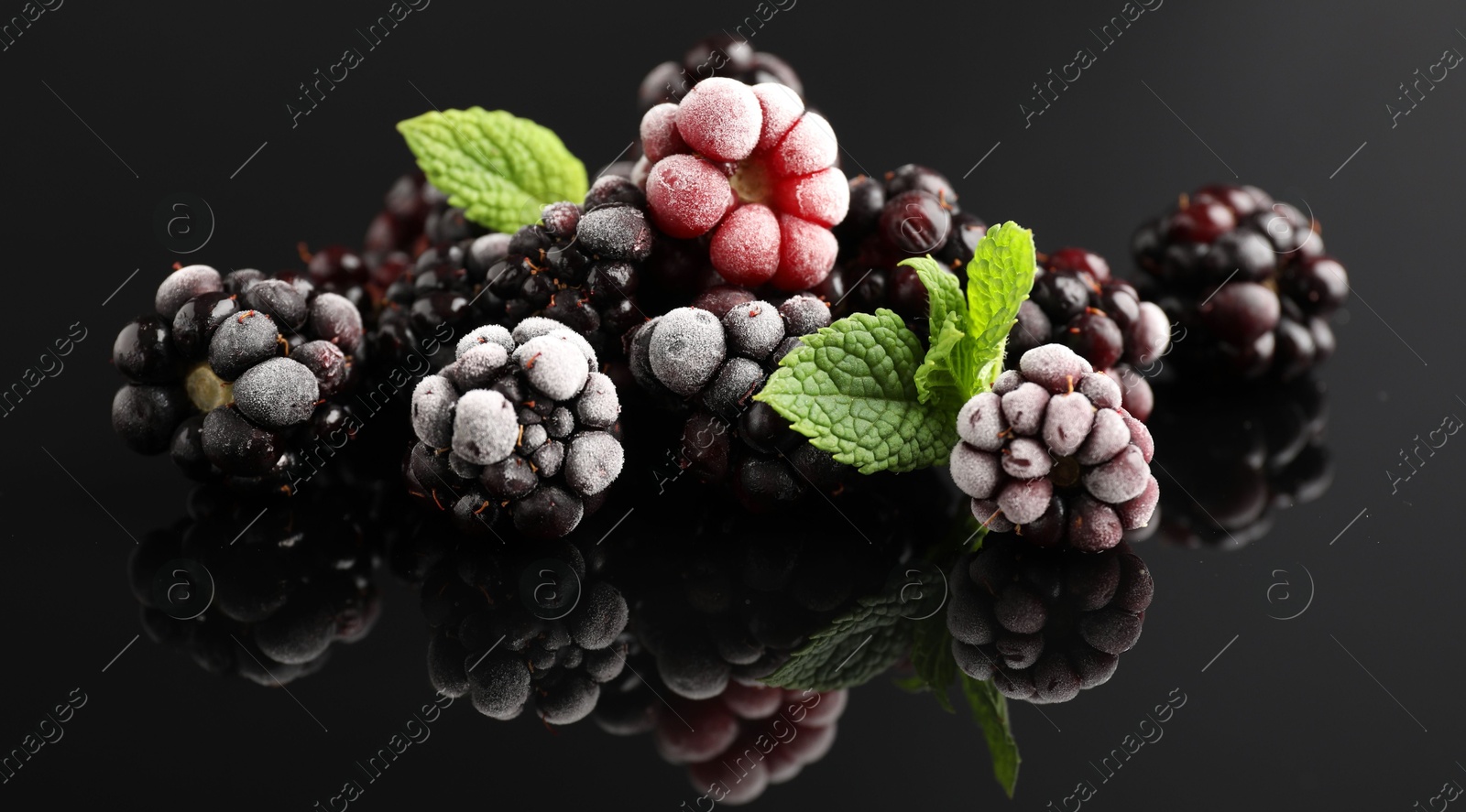 Photo of Frozen blackberries and mint on black table, closeup