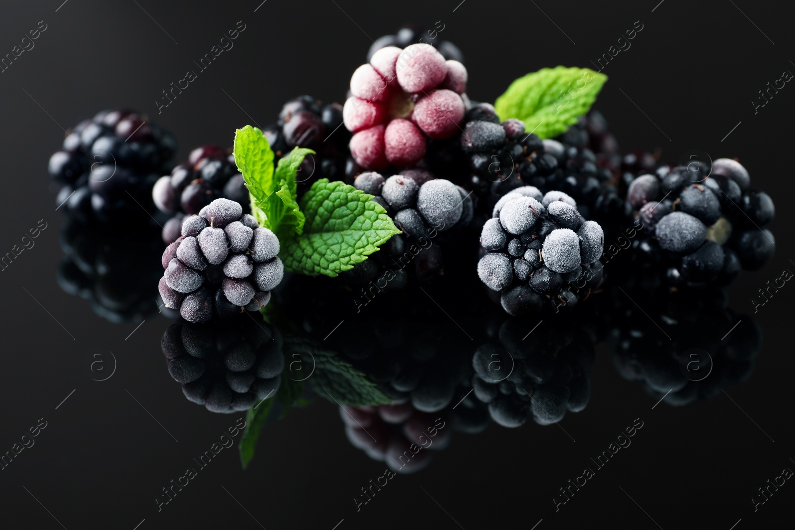 Photo of Frozen blackberries and mint on black table, closeup