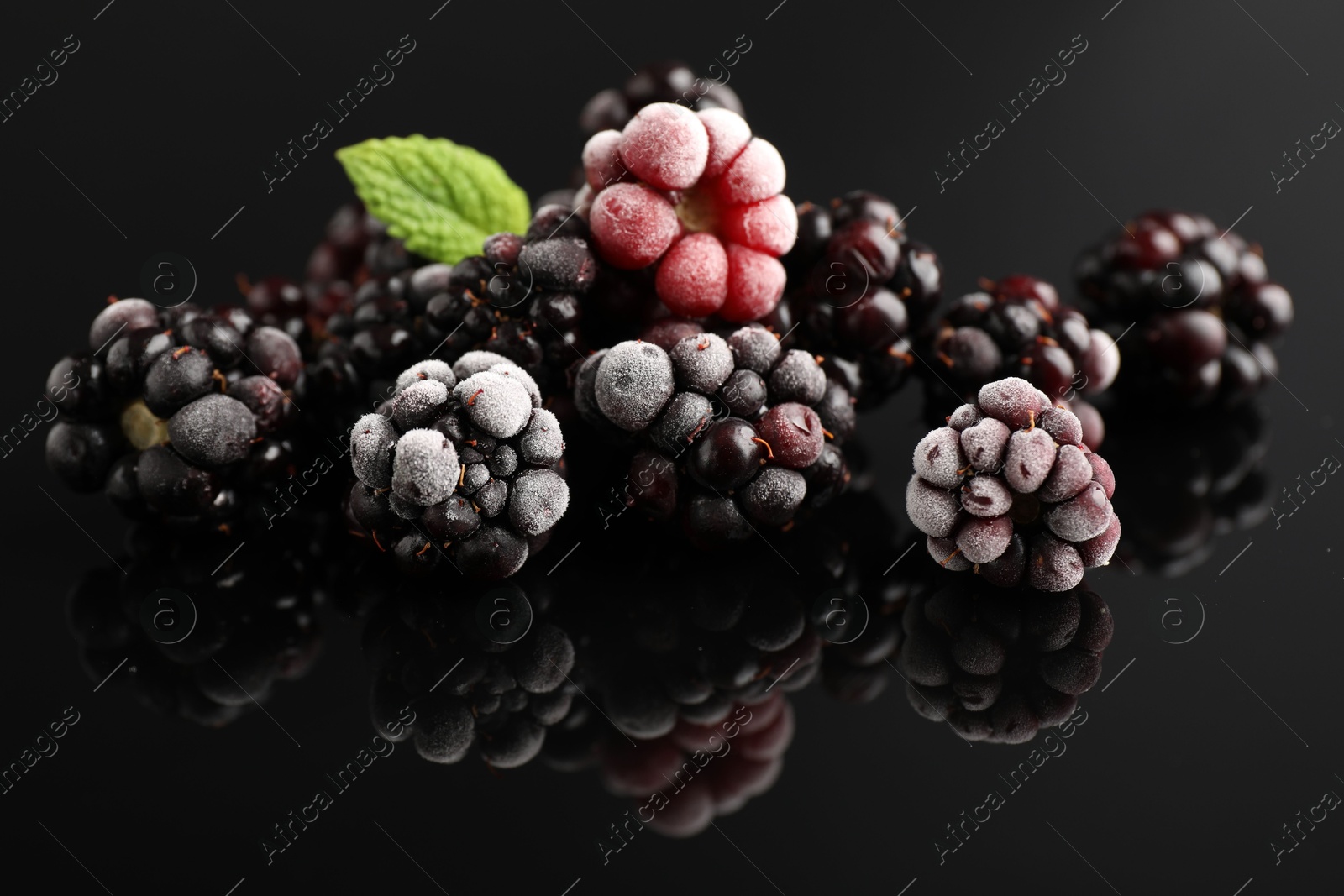 Photo of Frozen blackberries and mint on black table, closeup