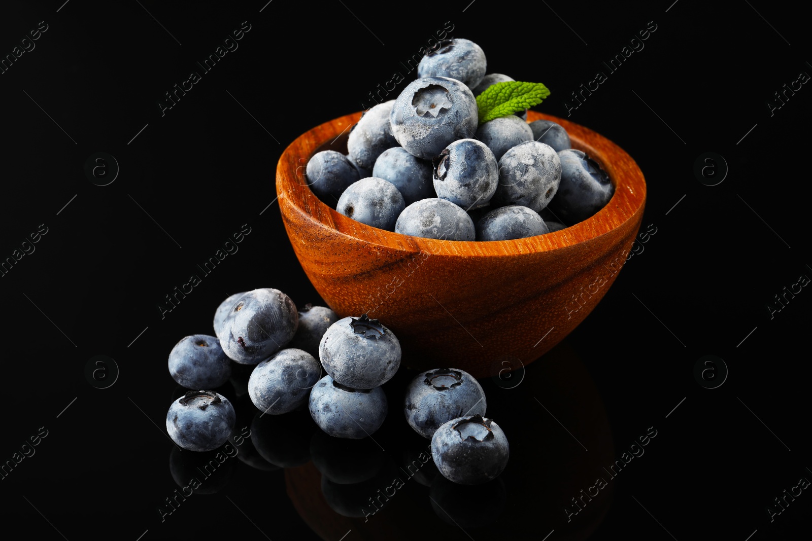 Photo of Many frozen blueberries in bowl on black table, closeup
