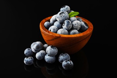 Photo of Many frozen blueberries in bowl on black table, closeup