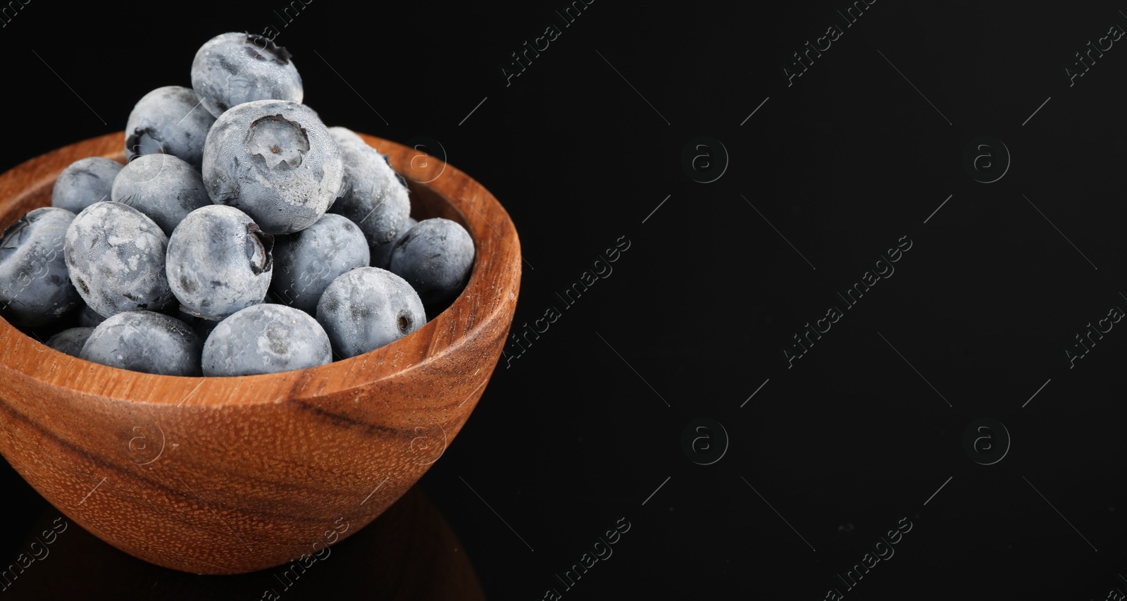 Photo of Many frozen blueberries in bowl on black table, closeup. Space for text