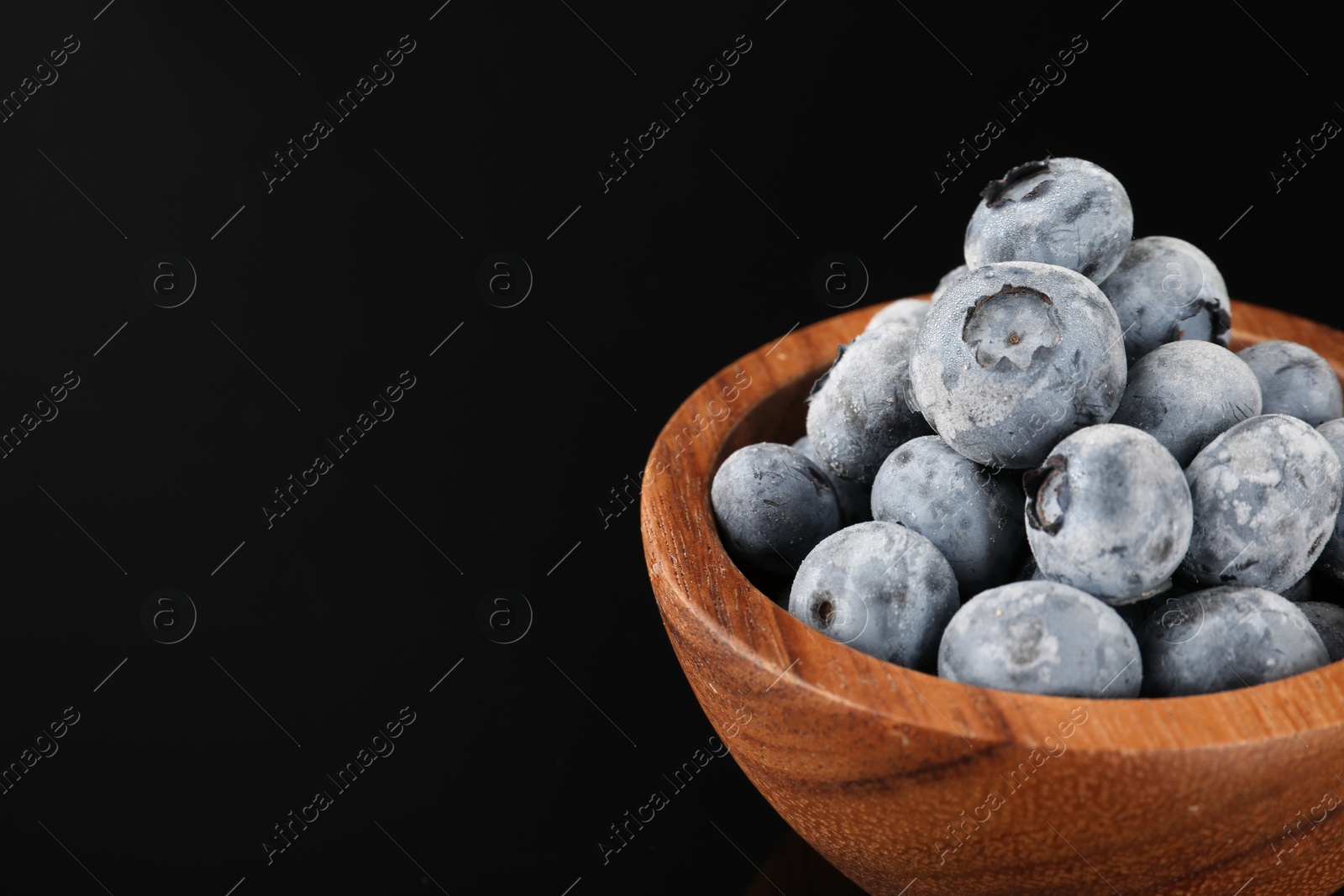 Photo of Many frozen blueberries in bowl on black table, closeup. Space for text