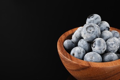 Photo of Many frozen blueberries in bowl on black table, closeup. Space for text