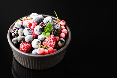 Photo of Many different frozen berries and mint in bowl on black table, closeup. Space for text