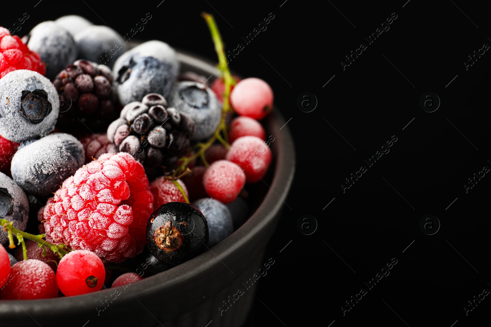 Photo of Many different frozen berries in bowl on black table, closeup. Space for text