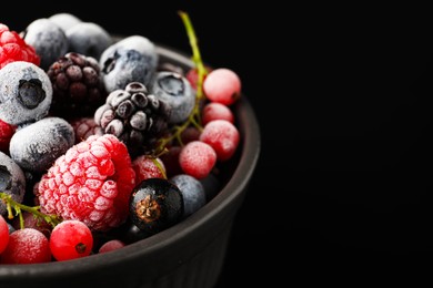 Photo of Many different frozen berries in bowl on black table, closeup. Space for text